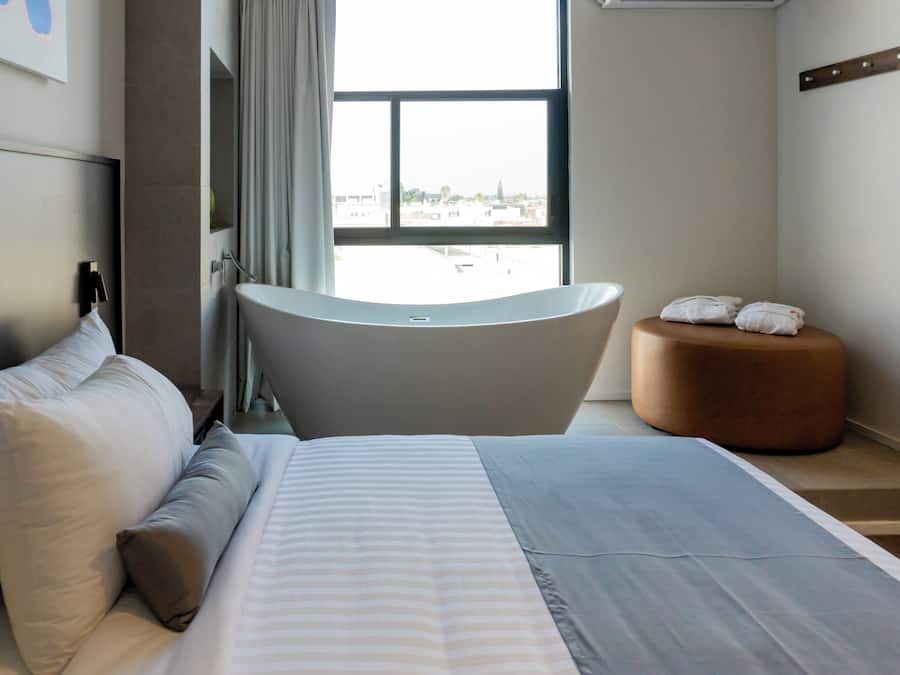 A modern hotel room with a large bed, a bathtub, and a view of the city.