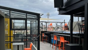 An outdoor seating area with tables and chairs, a patterned floor, and a view of the cityscape. - ALT Urbana (León)