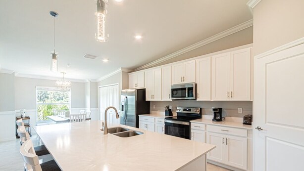 A modern kitchen with white cabinetry, stainless steel appliances, and a large island with a sink.