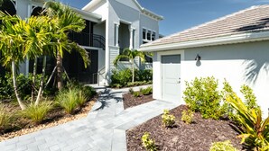 A modern two-story house with a covered patio, a garage, and a well-maintained garden with various plants and a paved walkway.