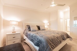 A bedroom with a bed, nightstands, a ceiling fan, and a door leading to another room.