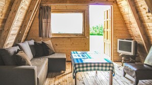 Ett mysigt rum på vinden med trägolv, en soffa, ett bord med en rutig duk, en tv och ett fönster med gardiner.