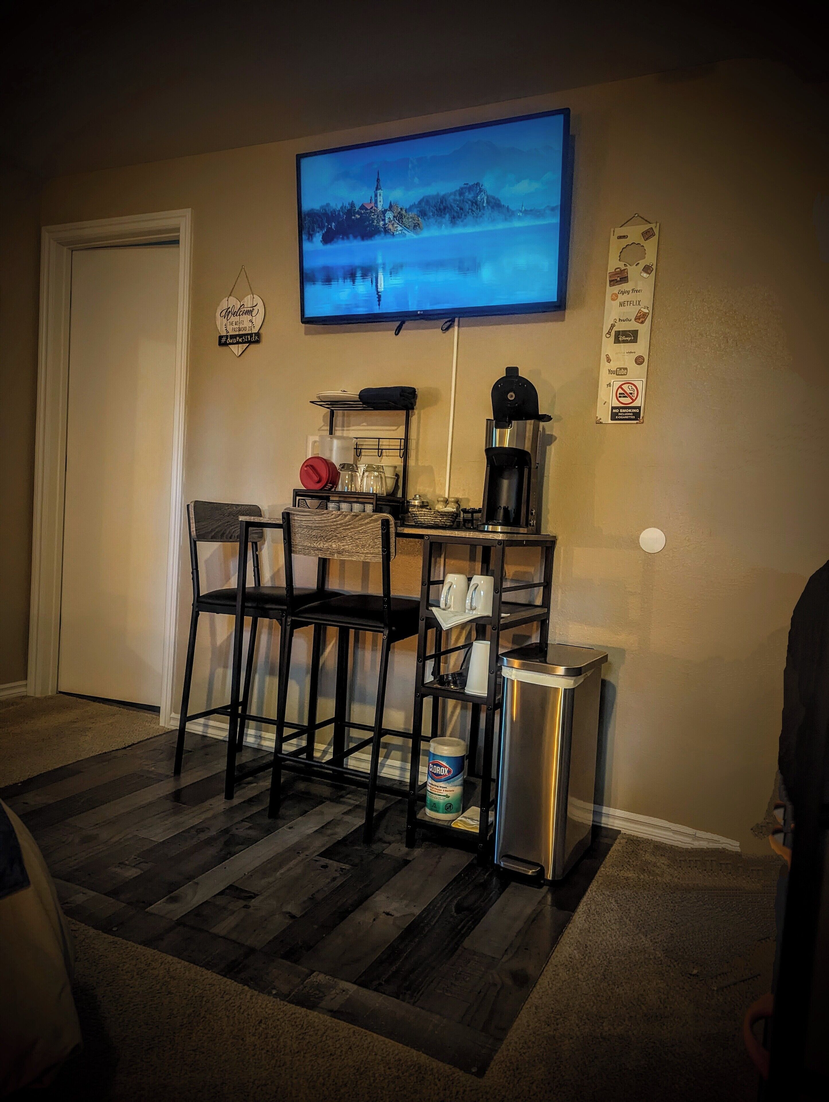 A cozy living room with a TV mounted on the wall, a coffee machine, and a small dining area with chairs and a table.