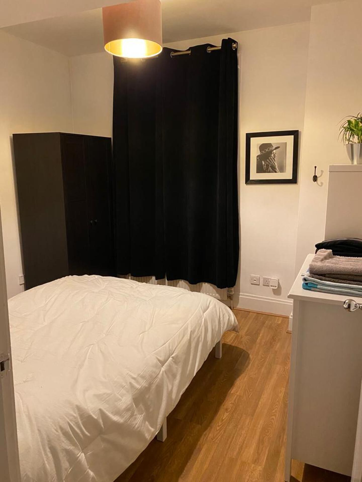 A bedroom with a bed, a wardrobe, a desk with a plant, and a framed picture on the wall.