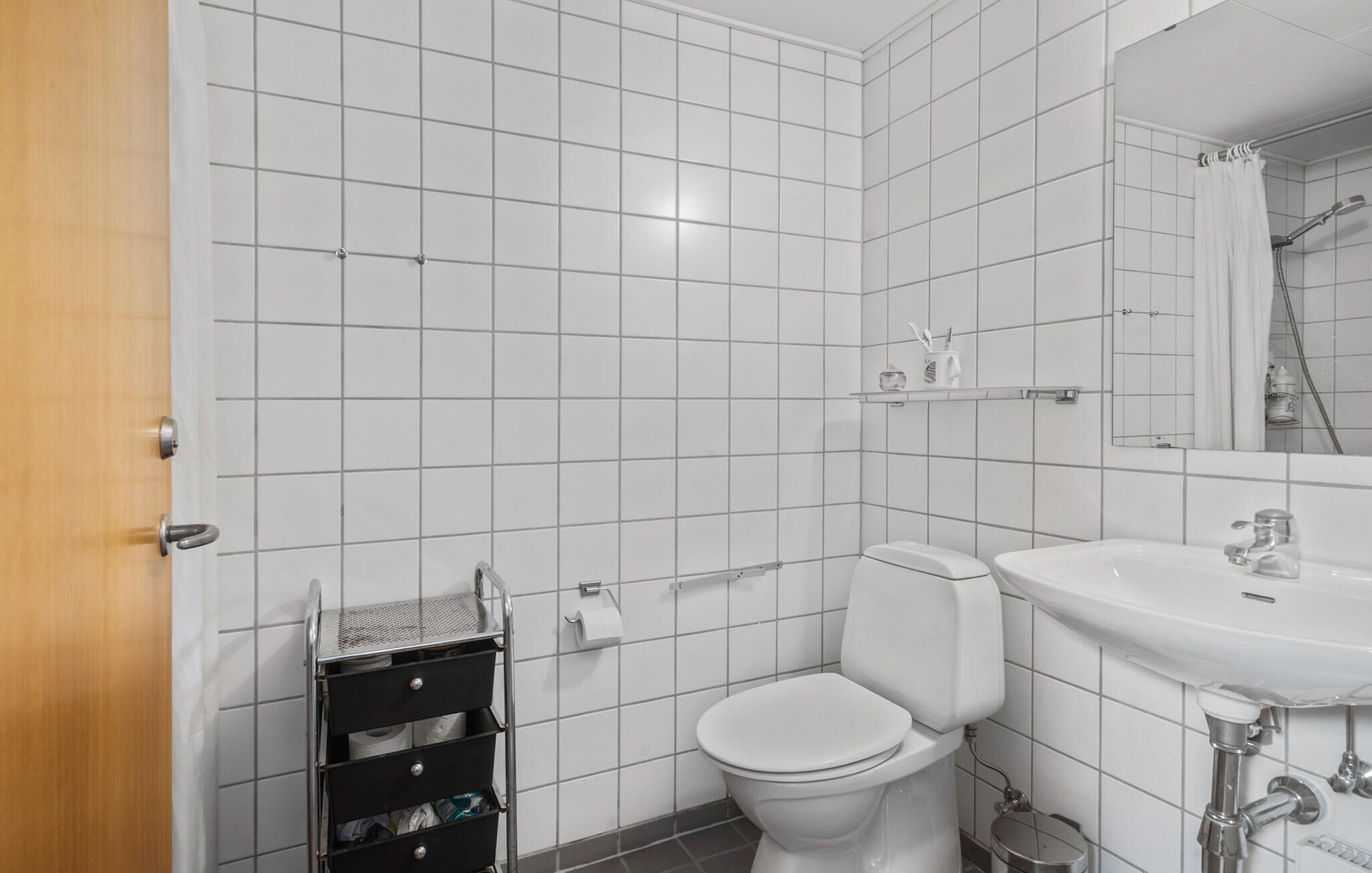 A bathroom with white tiled walls, a white toilet, a sink, and a mirror.