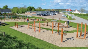 Ein Spielplatz mit verschiedenen Spielgeräten, einem Parkplatz und einem Gebäude mit Beschilderung.