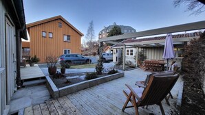 A wooden deck with outdoor furniture, a covered patio area, and a view of a residential building with a car parked in the driveway. - Mercury House, Cathedral View! Free parking! (Trøndelag)
