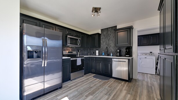 A modern kitchen with dark cabinets, stainless steel appliances, and a wooden floor. - 'Little Elm Diamond' - Steps to Lewisville Lake! (Little Elm)