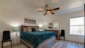 A bedroom with a wooden bed, two chairs, a standing lamp, a ceiling fan, and a large window. - 'Little Elm Diamond' - Steps to Lewisville Lake! (Little Elm)