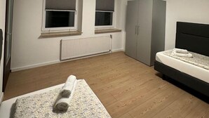 A bedroom with a bed, two windows, a wardrobe, and a radiator. - Studio Apartment für 2 - Guestrooms24 - Marl (Marl)