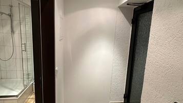 Un pasillo estrecho con un área de ducha a la izquierda y una puerta a la derecha.