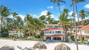 A beachfront hotel with multiple buildings, palm trees, and thatched umbrellas on the sand. - Casa Caribe: NEW beachfront, oceanview condo w/ housekeeper & rooftop terrace (Punta Cana)
