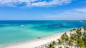 A beach with clear turquoise waters, a sandy shore, and palm trees. - Casa Caribe: NEW beachfront, oceanview condo w/ housekeeper & rooftop terrace (Punta Cana)
