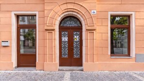A building facade with a central arched entrance, two side windows, and a small sign above the entrance.