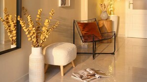 A modern interior with a white sofa, a black metal chair, and a white pouf. There are framed artworks on the wall and a vase with dried plants.