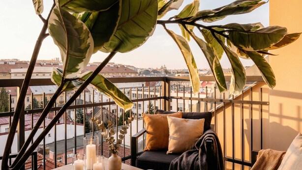 A balcony with a view of the city, a table with candles, a book, and a sofa with cushions.