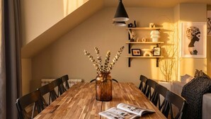 A dining area with a wooden table, black chairs, a vase with branches, and a hanging pendant light.