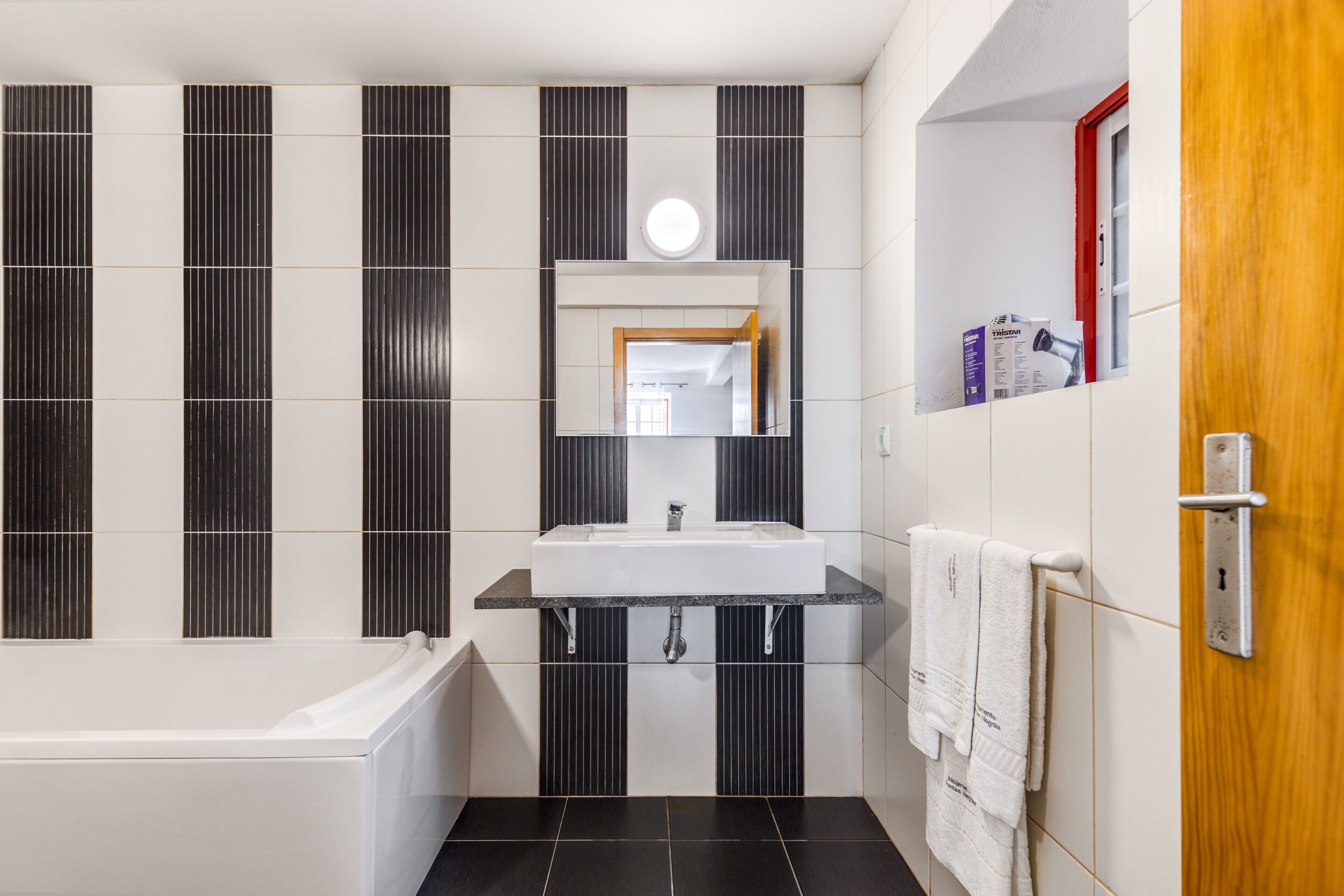 Un baño moderno con bañera, lavabo con espejo y un perchero para toallas.