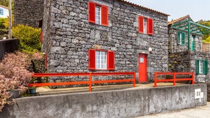 Un edificio de piedra con contraventanas rojas y un banco de hormigón.