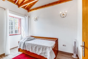A bedroom with a wooden bed, white curtains, a red-framed window, two wall-mounted lights, and a standing heater.