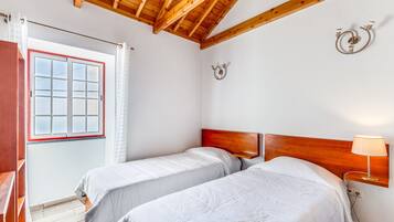 Un dormitorio con dos camas, techo de madera, ventana con cortinas y una lámpara fijada a la pared.
