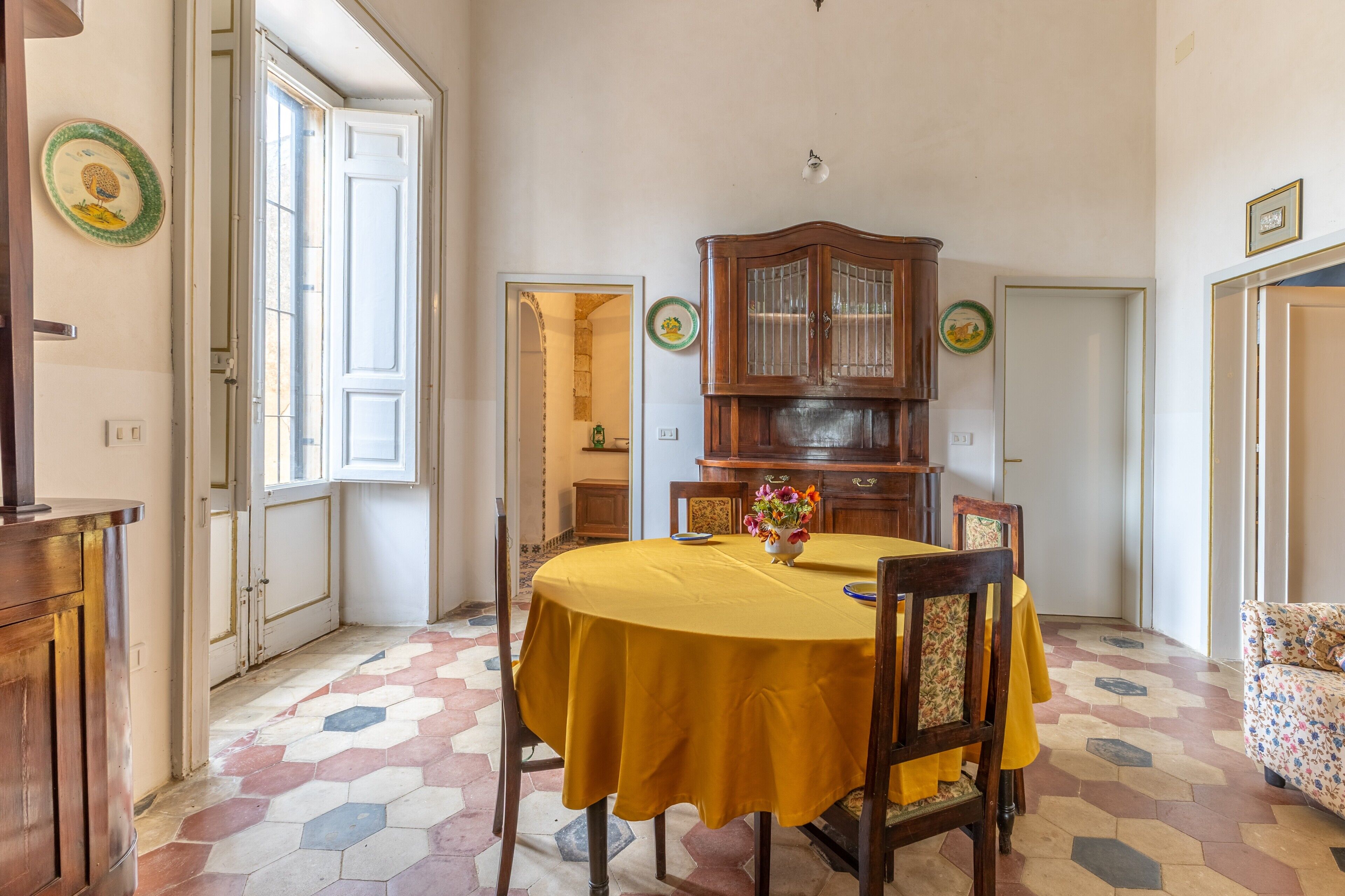 Ein Essbereich mit einem runden Tisch, Stühlen, einem Holzschrank und einem gemusterten Boden.