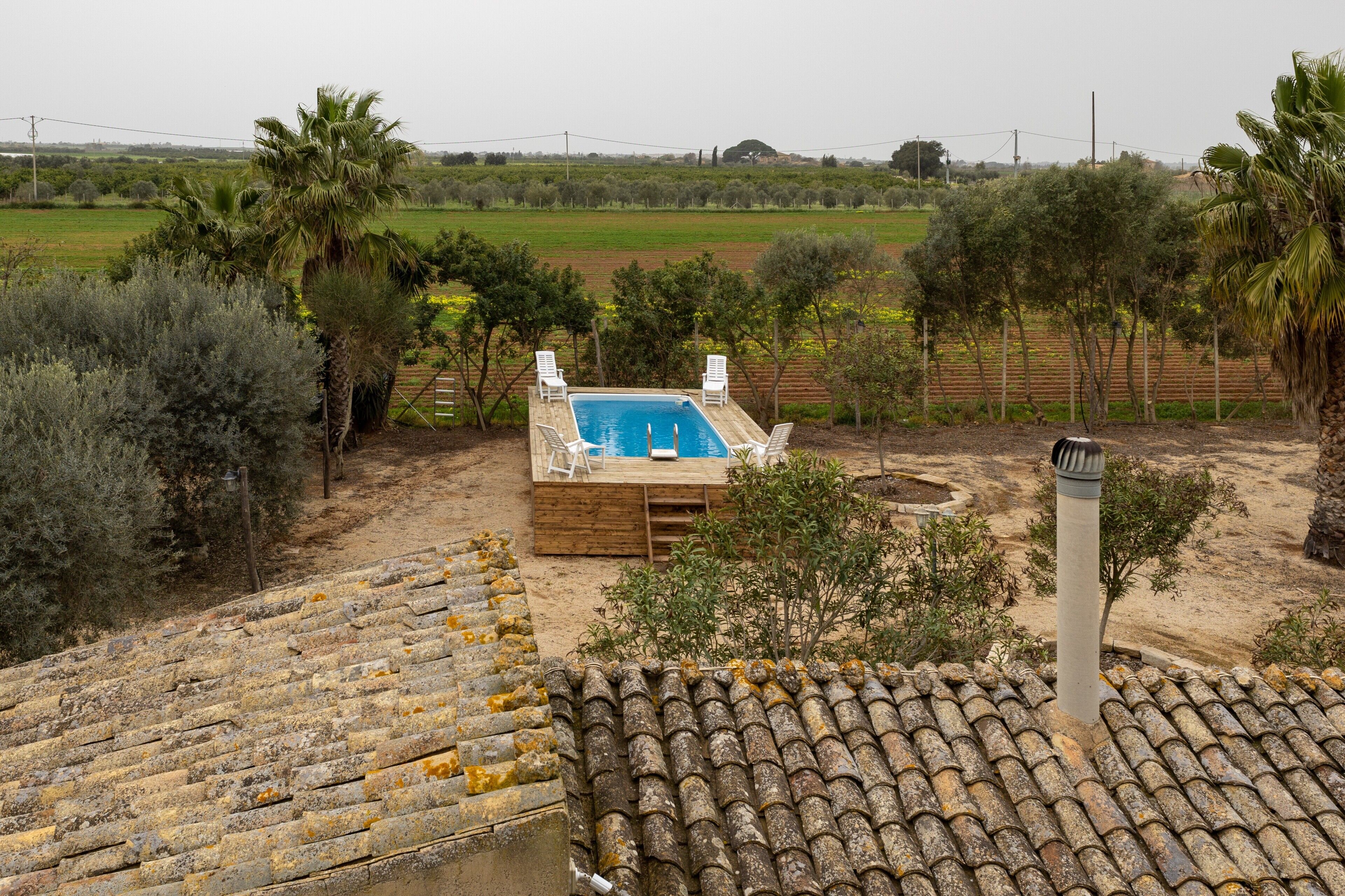 A swimming pool with two white lounge chairs, surrounded by trees and a field.