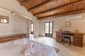 A bedroom with a wooden ceiling, a bed with white linens, a desk with drawers, and a chair.