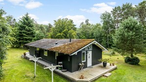 Una cabaña pequeña con terraza de madera, rodeada de césped y árboles.
