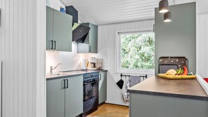 Una cocina moderna con armarios verde claro, horno empotrado y ventana con vistas a vegetación.