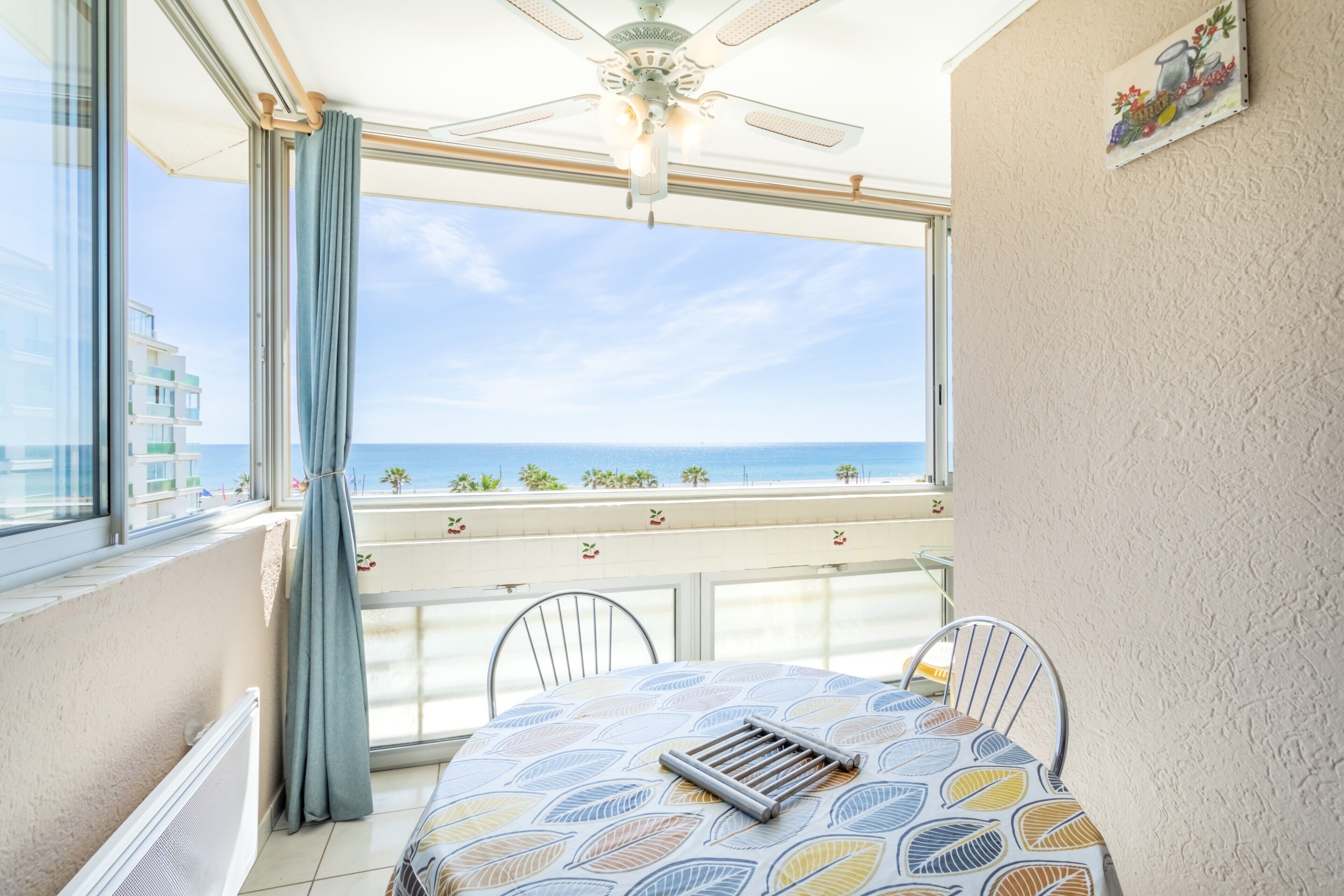 A balcony with a table and chairs, a ceiling fan, and a view of the sea.