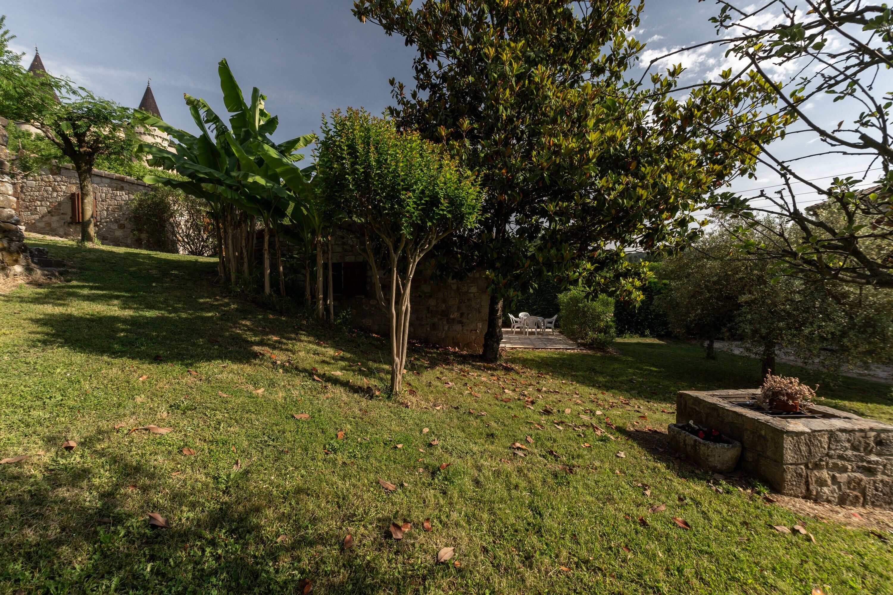 A stone building with a grassy area, a tree, and a small table with a planter.