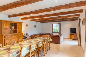 Un espace repas avec une longue table, des meubles de rangement en bois et un téléviseur en arrière-plan.