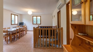 A dining area with a wooden table and chairs, a television, and a staircase leading to an upper level. - Les Sources Gite Cabernet House with Shared Pool, Private Terrace, and Air Conditioning (Chambonas)