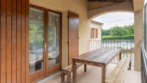 A wooden table and bench on a balcony with a view of greenery and a building in the background. - Les Sources Gite Cabernet House with Shared Pool, Private Terrace, and Air Conditioning (Chambonas)