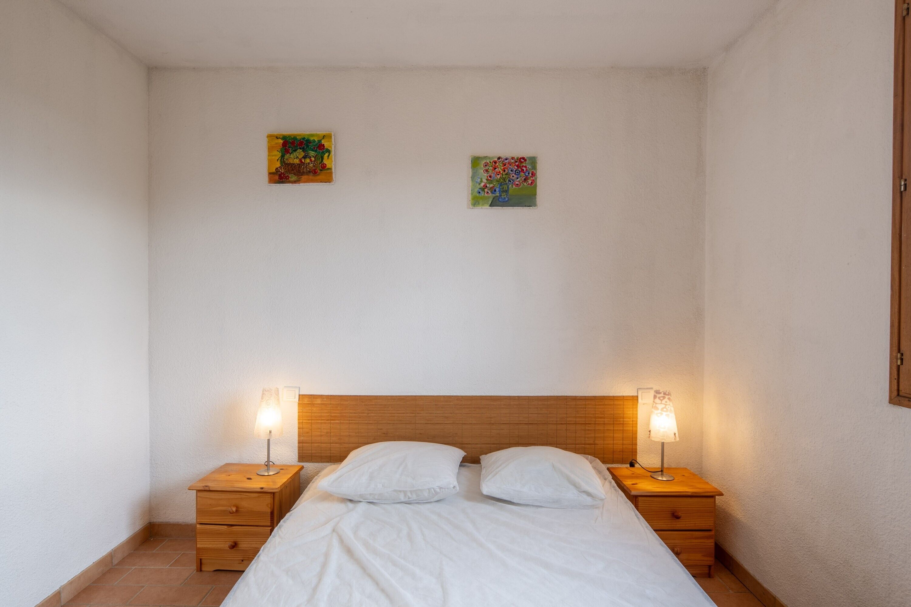 Una cama pequeña y ordenada con dos almohadas blancas y dos mesitas de noche con lámparas.