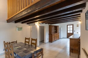 A dining area with a wooden table and chairs, a kitchen with a microwave, and a wooden cabinet. - Charming 'Les Sources Gîte La Grange' House with Shared Pool and Private Terrace (Chambonas)