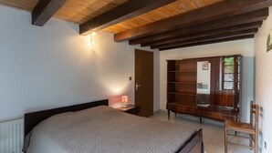A bedroom with a bed, a wooden wardrobe, a nightstand with a lamp, and a wooden chair. - Charming 'Les Sources Gîte La Grange' House with Shared Pool and Private Terrace (Chambonas)