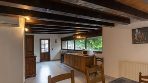 A kitchen with wooden cabinets, a tiled floor, a dining table with chairs, and a window with a view of greenery. - Charming 'Les Sources Gîte La Grange' House with Shared Pool and Private Terrace (Chambonas)