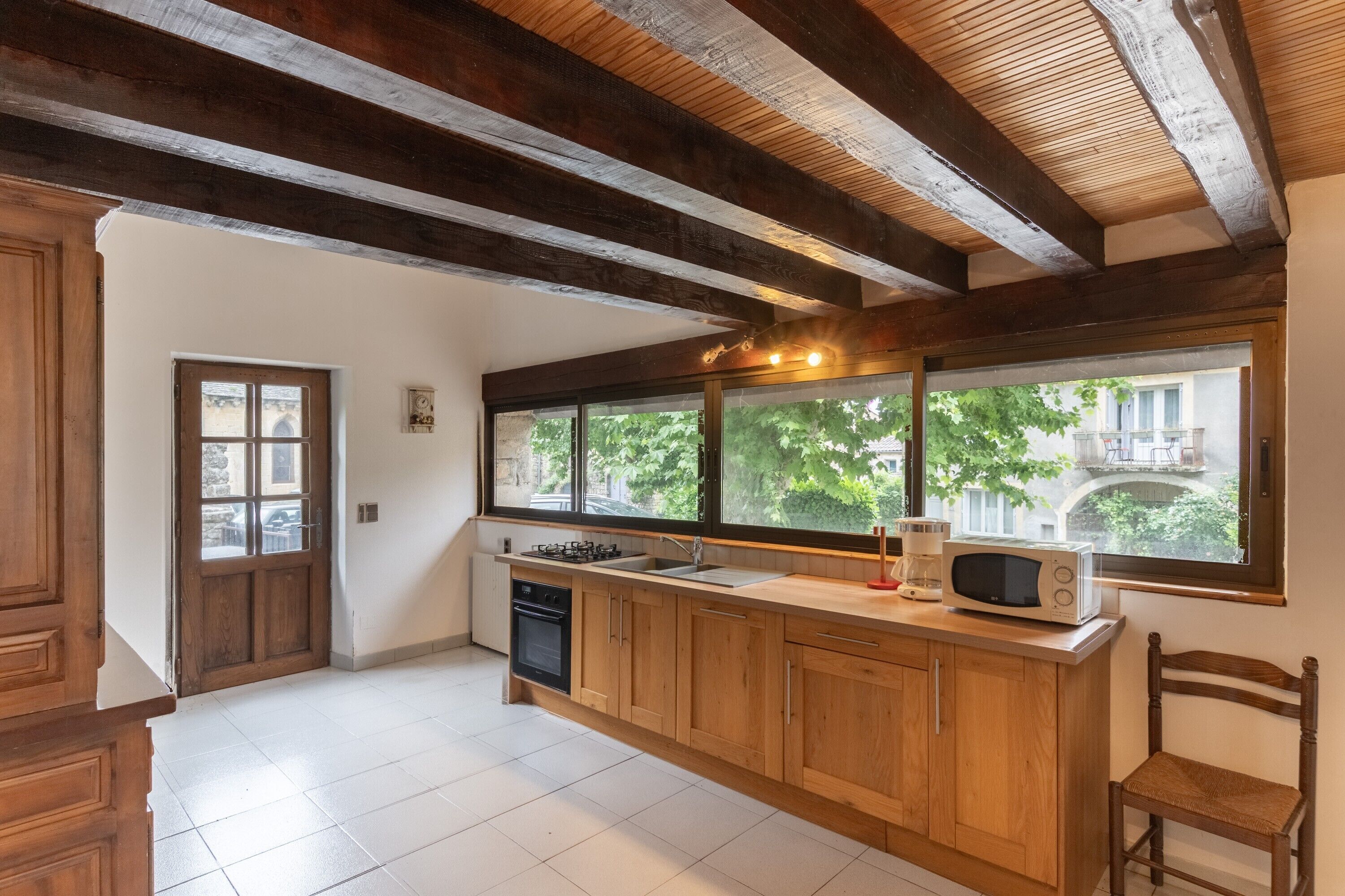 Una cocina con armarios de madera, microondas y ventana con vista a zonas verdes y edificios.