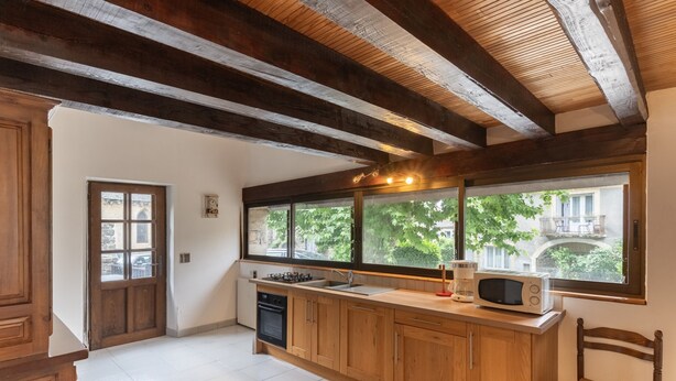 A kitchen with wooden cabinets, a microwave, and a window with a view of greenery and buildings. - Charming 'Les Sources Gîte La Grange' House with Shared Pool and Private Terrace (Chambonas)