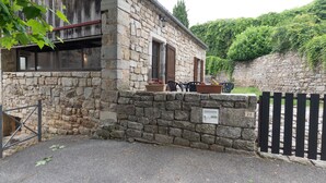 A stone building with a wooden door, a small outdoor seating area with a table and chairs, and a gate. - Charming 'Les Sources Gîte La Grange' House with Shared Pool and Private Terrace (Chambonas)