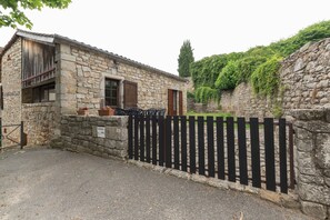 A stone building with a wooden door, a black fence, and a paved area. - Charming 'Les Sources Gîte La Grange' House with Shared Pool and Private Terrace (Chambonas)