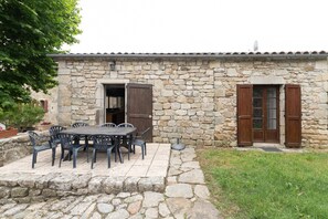 A stone building with a patio table and chairs, a door, and a window. - Small House 'Les Sources Gîte La Grange' with Shared Pool, Private Terrace (Chambonas)