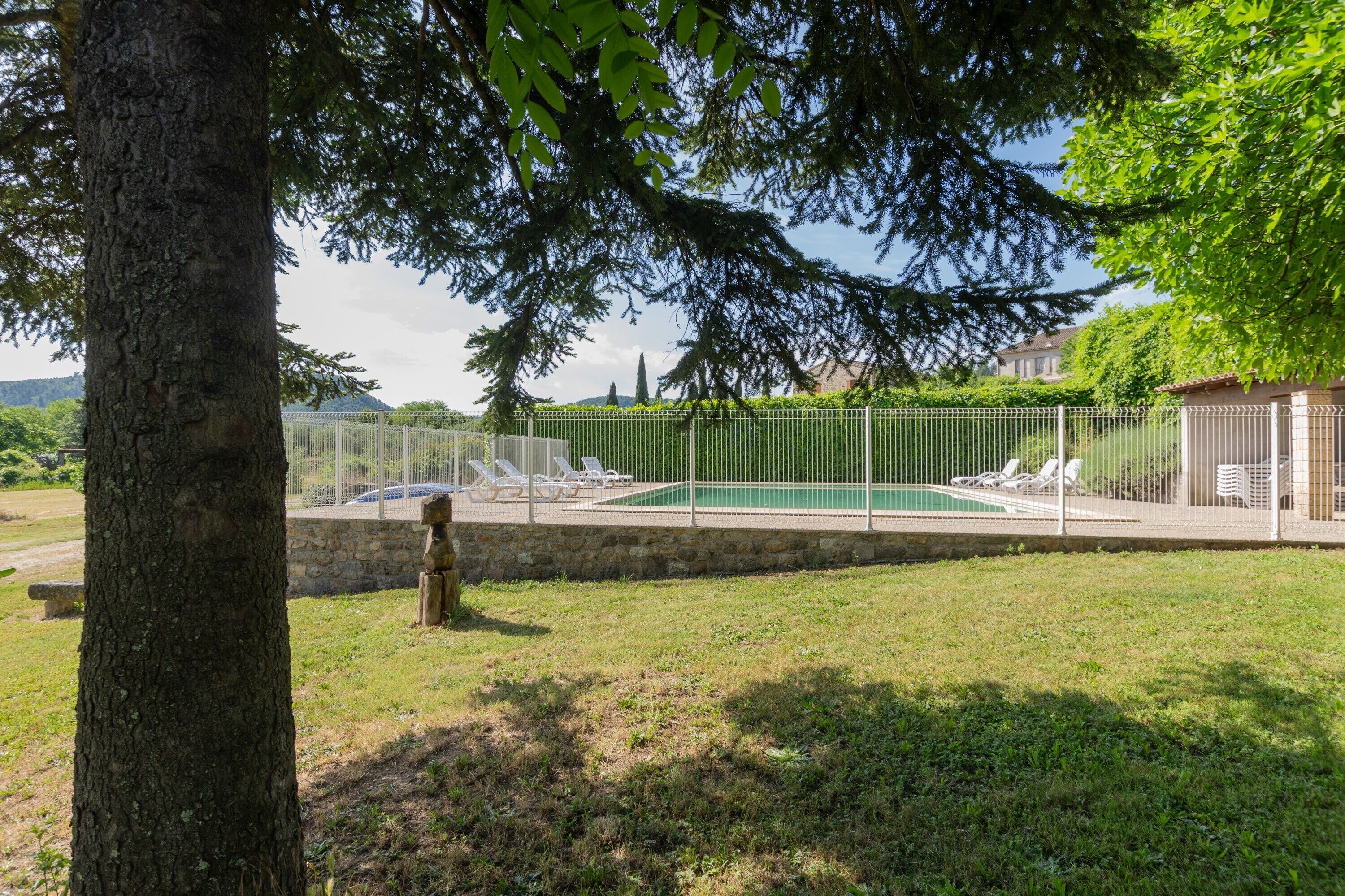 A fenced outdoor area with a pool, lounge chairs, and a stone wall.