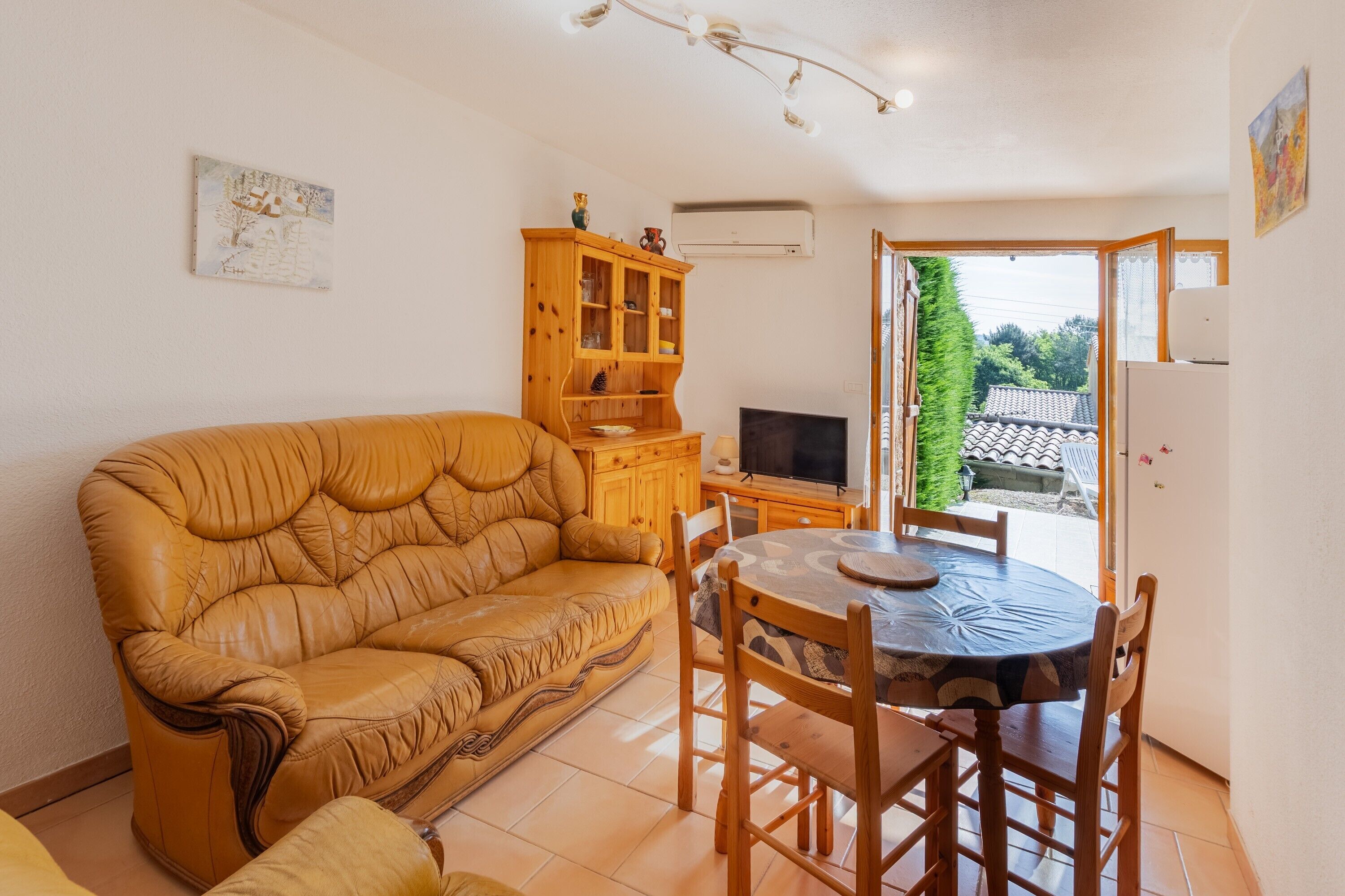 Un soggiorno con divano, tavolo da pranzo con sedie, televisore, mobiletto in legno e una finestra vista casa.