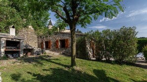 A stone building with a tree in front, a small structure with a chimney, and a clear sky. - 'Les Sources Gîte La Remise' House with Shared Pool, Private Terrace, and Air Conditioning (Chambonas)