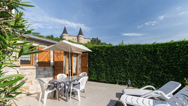 A patio with a table and chairs, a lounge area with sun loungers, and a castle in the background. - 'Les Sources Gîte La Remise' House with Shared Pool, Private Terrace, and Air Conditioning (Chambonas)