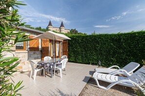 Eine Terrasse mit Tisch und Stühlen, eine Lounge-Bereich mit Liegestühlen und eine Burg im Hintergrund.