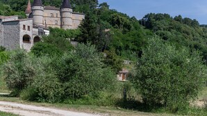 A historic castle with multiple towers, surrounded by dense greenery and a dirt path. - 'Les Sources Gîte La Remise' House with Shared Pool, Private Terrace, and Air Conditioning (Chambonas)
